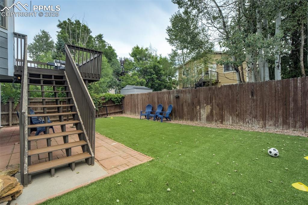 Image 31 of 36: Fenced backyard with stairs, a wooden deck, and a patio area