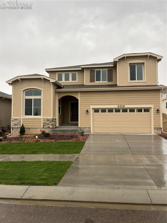 Caption: View of front of house featuring a garage, concrete driveway, stone siding, a front lawn, and a porc