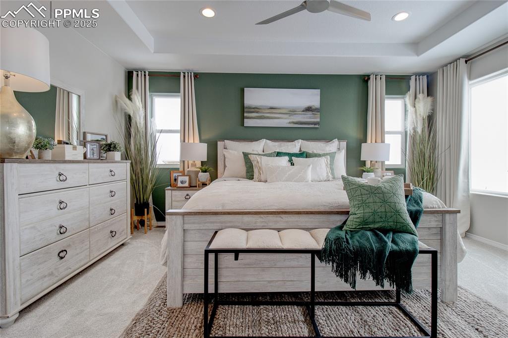 Image 23 of 32: Bedroom with light carpet, a tray ceiling, multiple windows, and recessed l