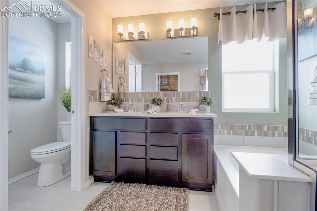 Image 26 of 32: Bathroom with double vanity, healthy amount of natural light, a bath, and b