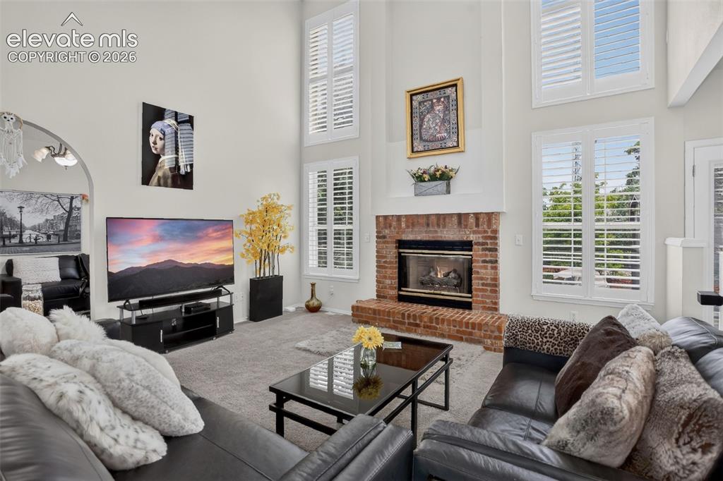 Image 21 of 49: Great room featuring a two-story ceiling, a brick fireplace, tall windows w