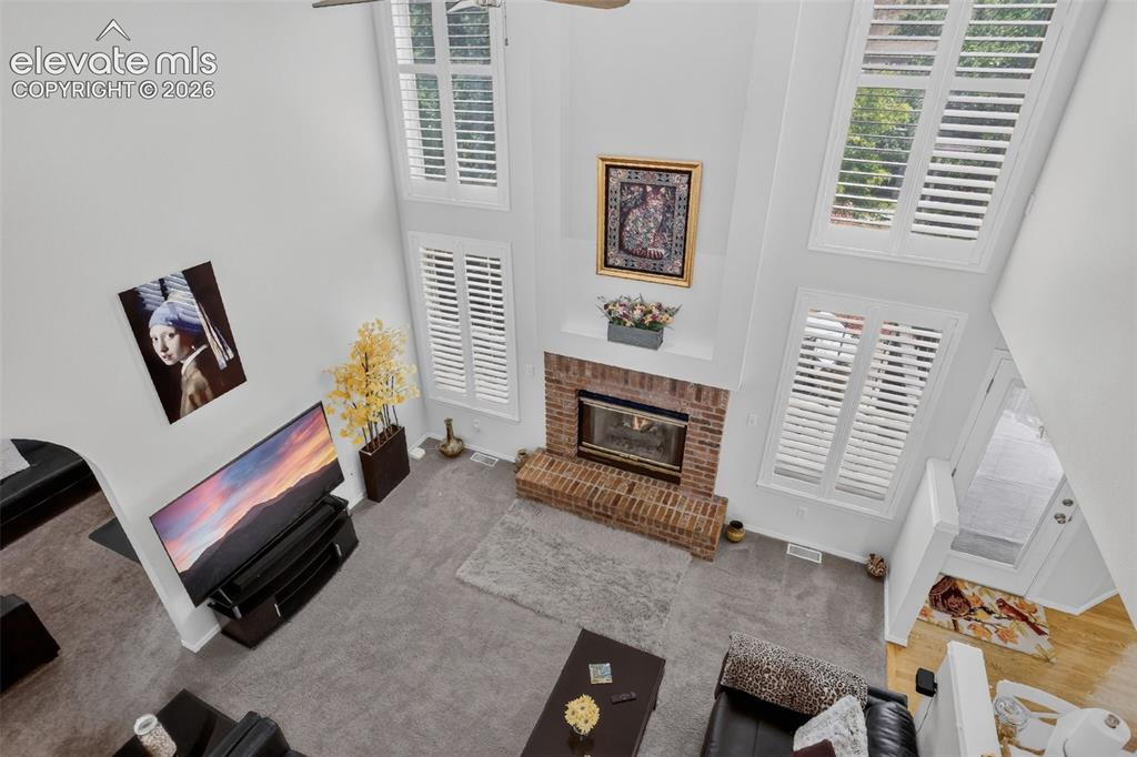Image 23 of 49: Two-story living area featuring a prominent brick fireplace with a white ma