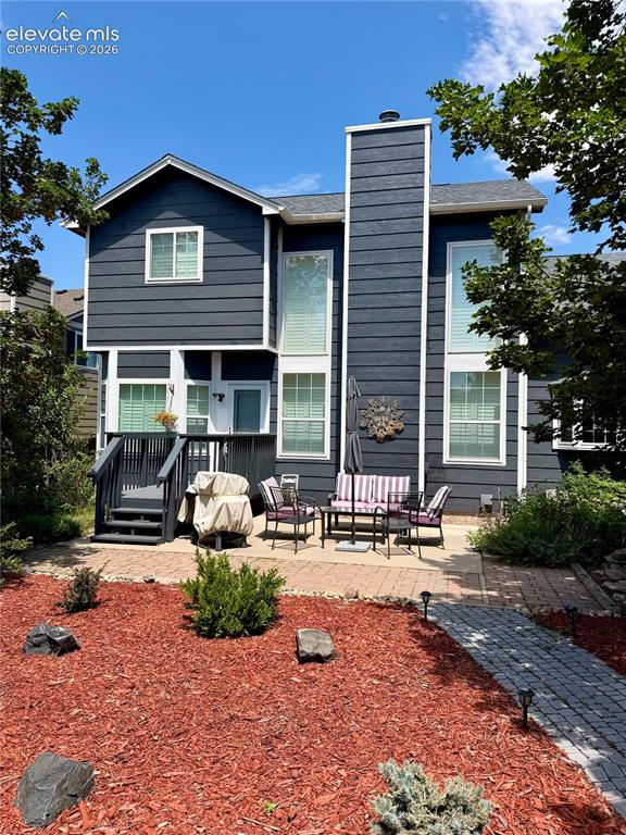 Image 32 of 49: Rear exterior featuring a multi-level deck, a spacious paver patio, mature