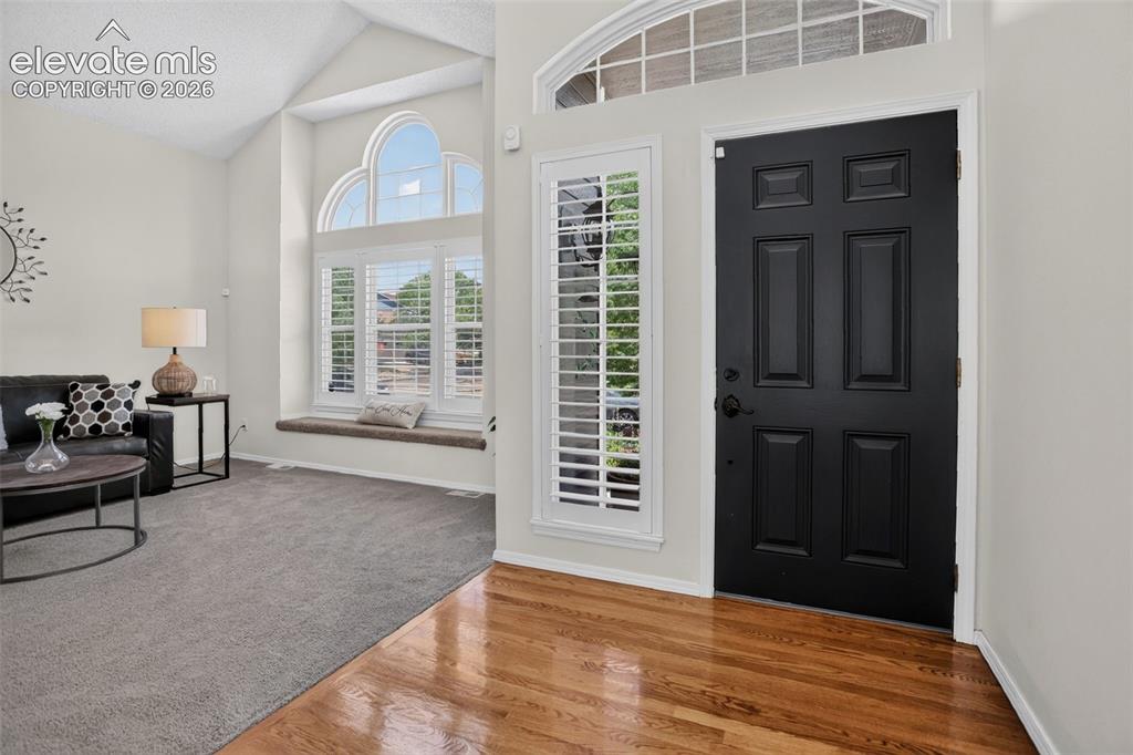 Image 6 of 49: Entryway featuring a paneled black door, hardwood flooring, and a transom w