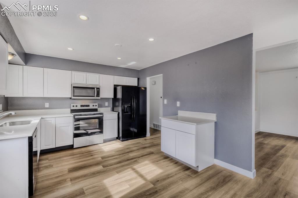 Image 13 of 36: Kitchen with black appliances, white cabinetry, light wood finished floors,