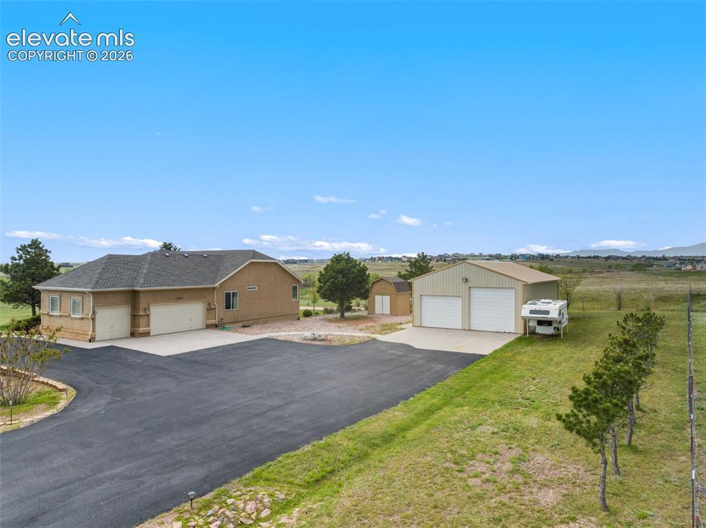 Image 2 of 49: Side entry of home with asphalt driveway, 3-car attached garage, small shed