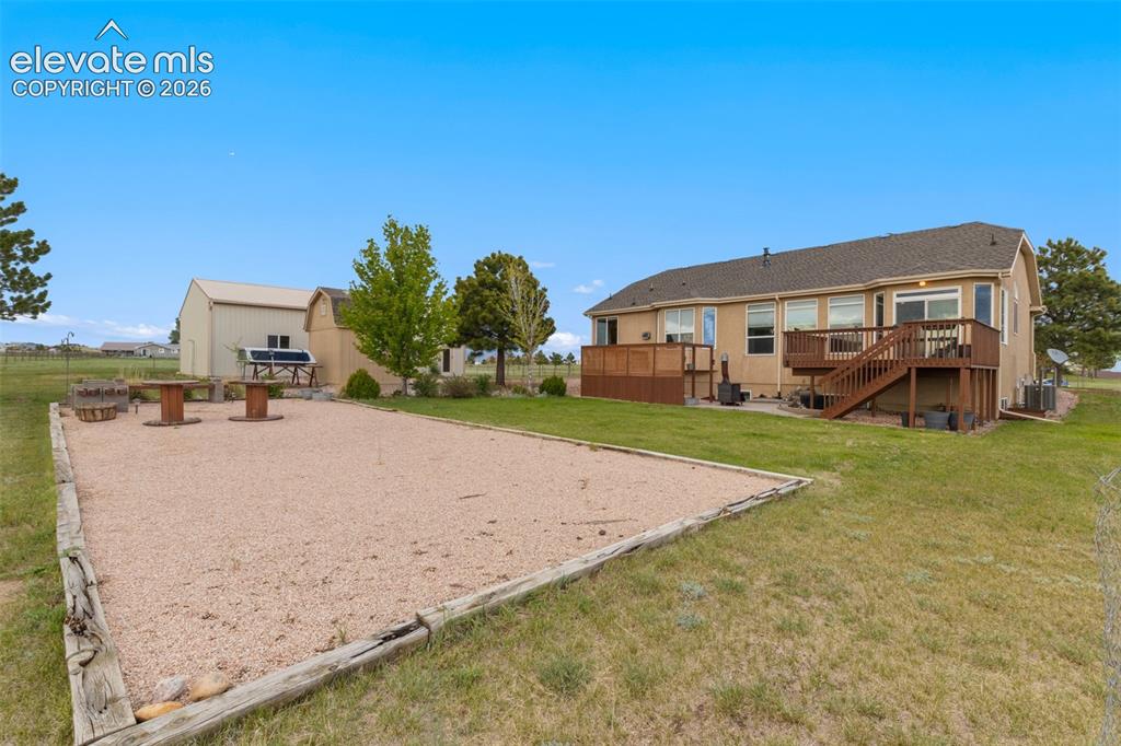 Image 39 of 49: Backside of the home showing deck, hot tub with privacy fence, gravel area,