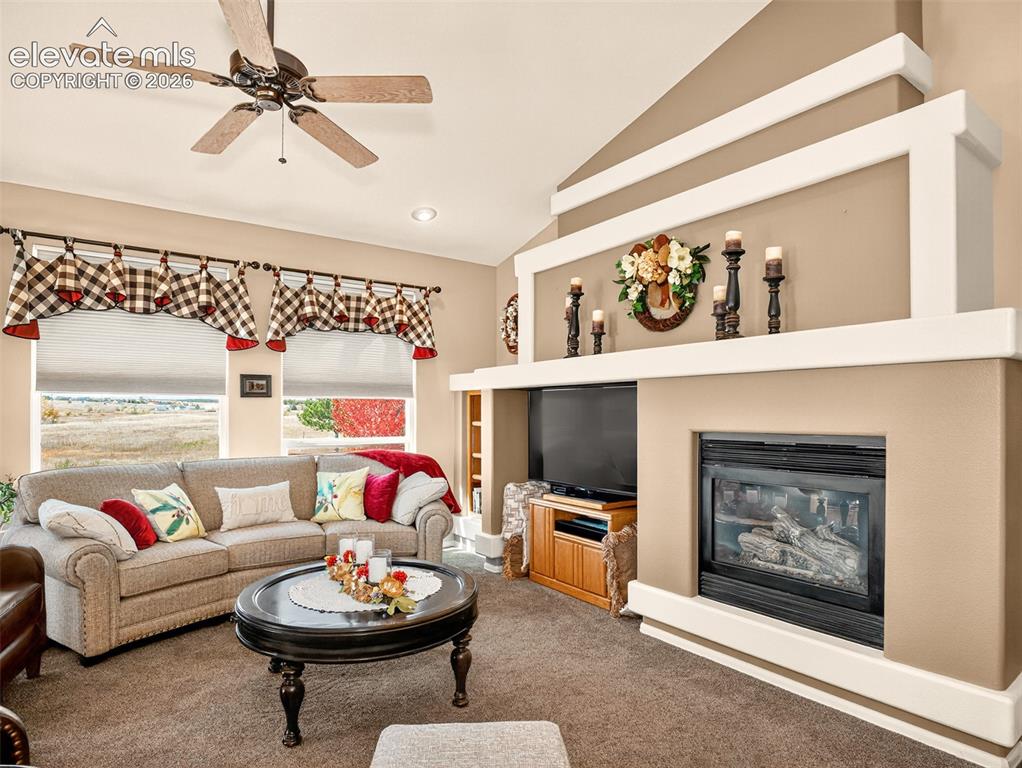 Image 5 of 49: Living room with gas fireplace, ceiling fan, carpet and large windows with