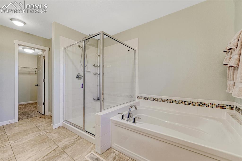 Image 19 of 50: Bathroom featuring a bath, a stall shower, and a walk in closet
