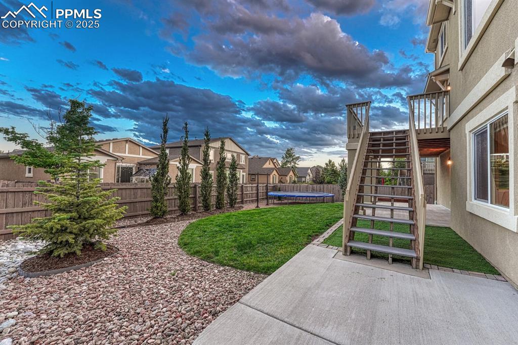 Image 32 of 50: Fenced backyard with a trampoline, stairway, a patio area, and a residentia