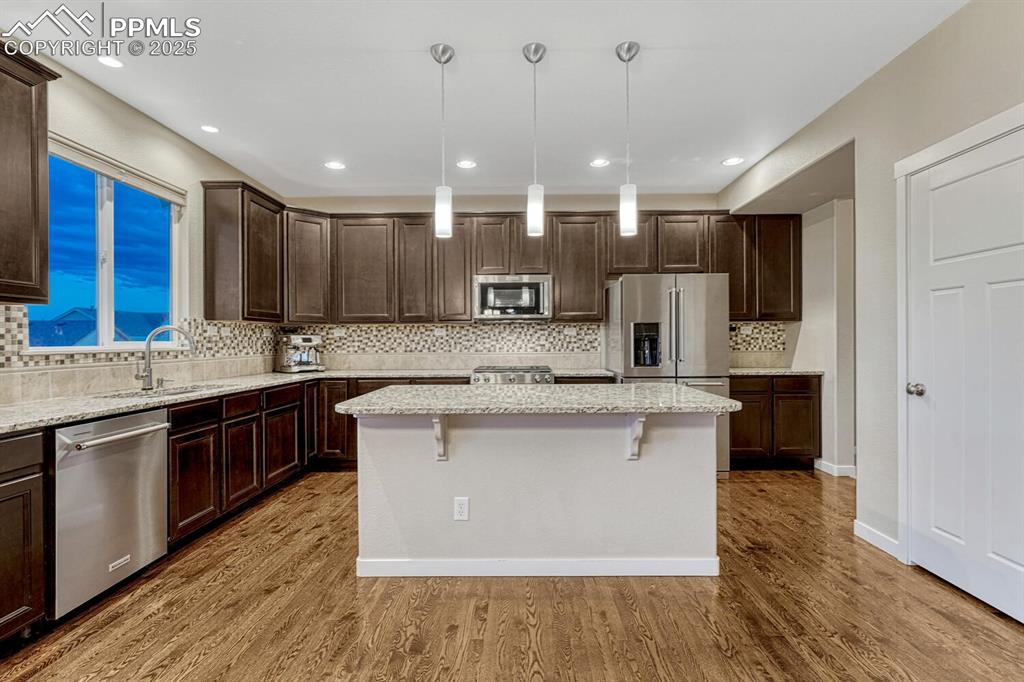 Image 6 of 50: Kitchen features a wood floor, island with bartop seating and pendant light