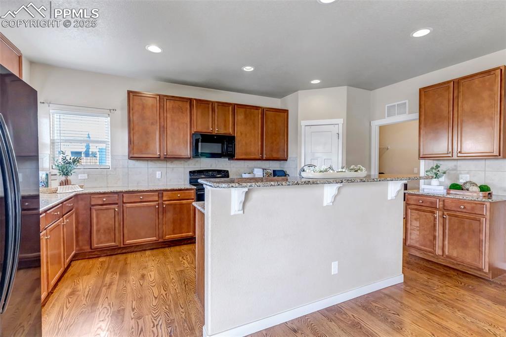 Image 11 of 37: Kitchen featuring backsplash, light stone countertops, brown cabinetry, a k