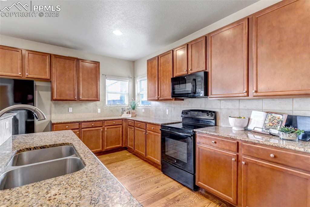 Image 12 of 37: Kitchen featuring brown cabinets, black appliances, light wood finished flo