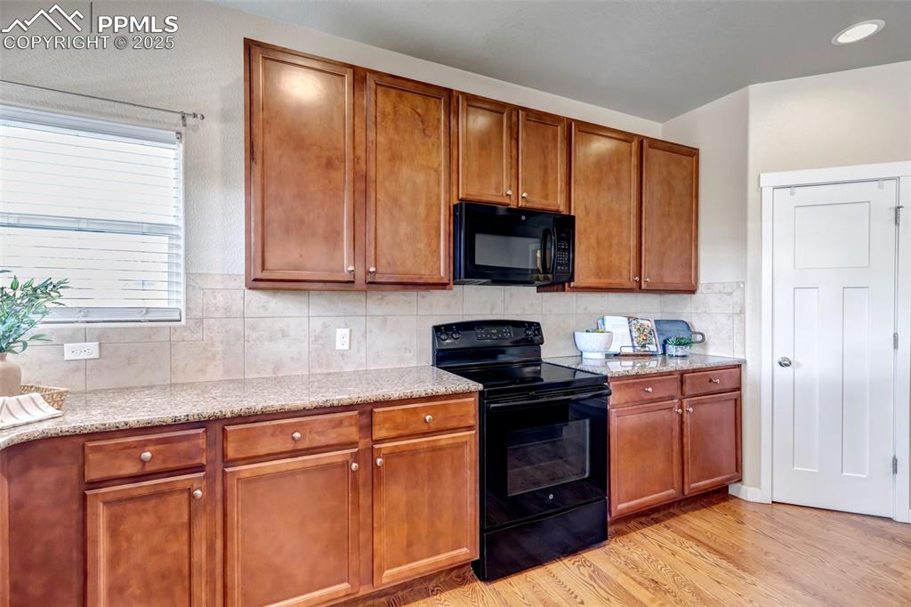 Image 13 of 37: Kitchen with brown cabinetry, black appliances, light stone countertops, li