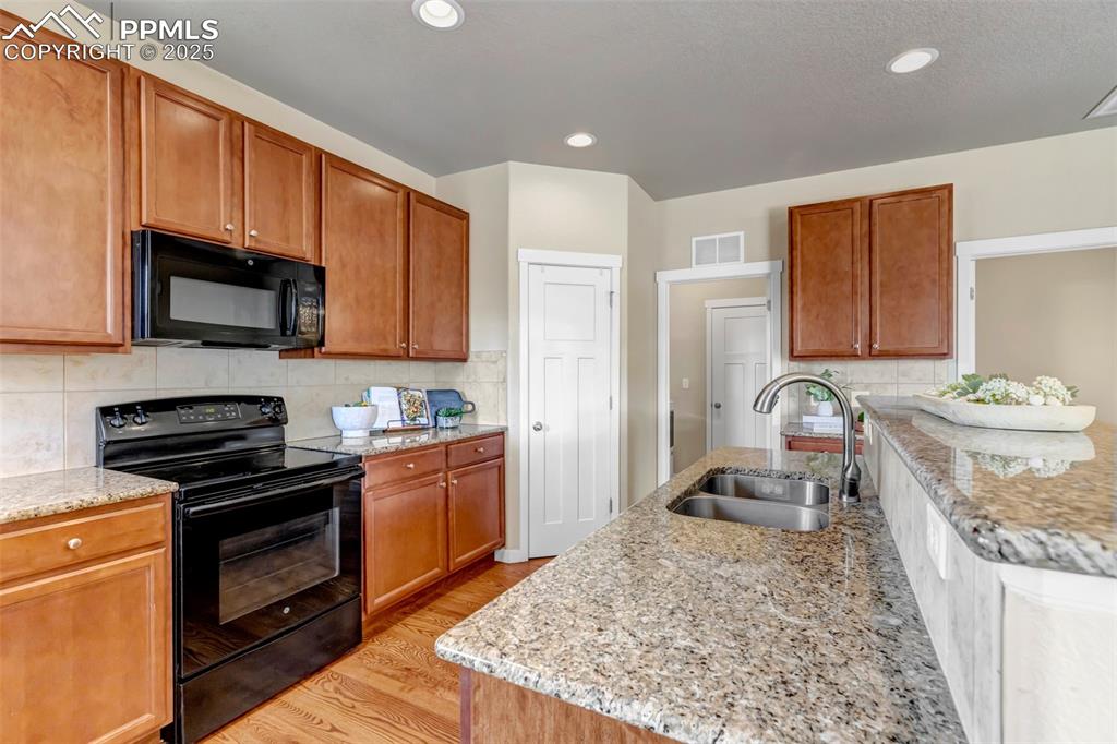Image 14 of 37: Kitchen featuring black appliances, light stone countertops, light wood-typ