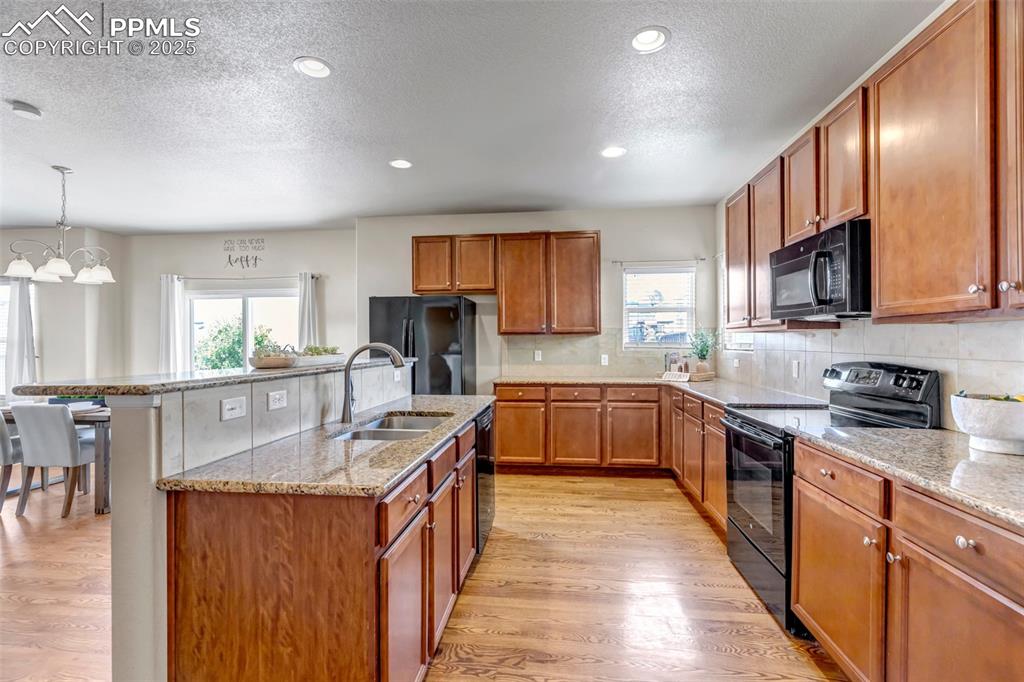 Image 15 of 37: Kitchen featuring black appliances, brown cabinetry, light stone counters,