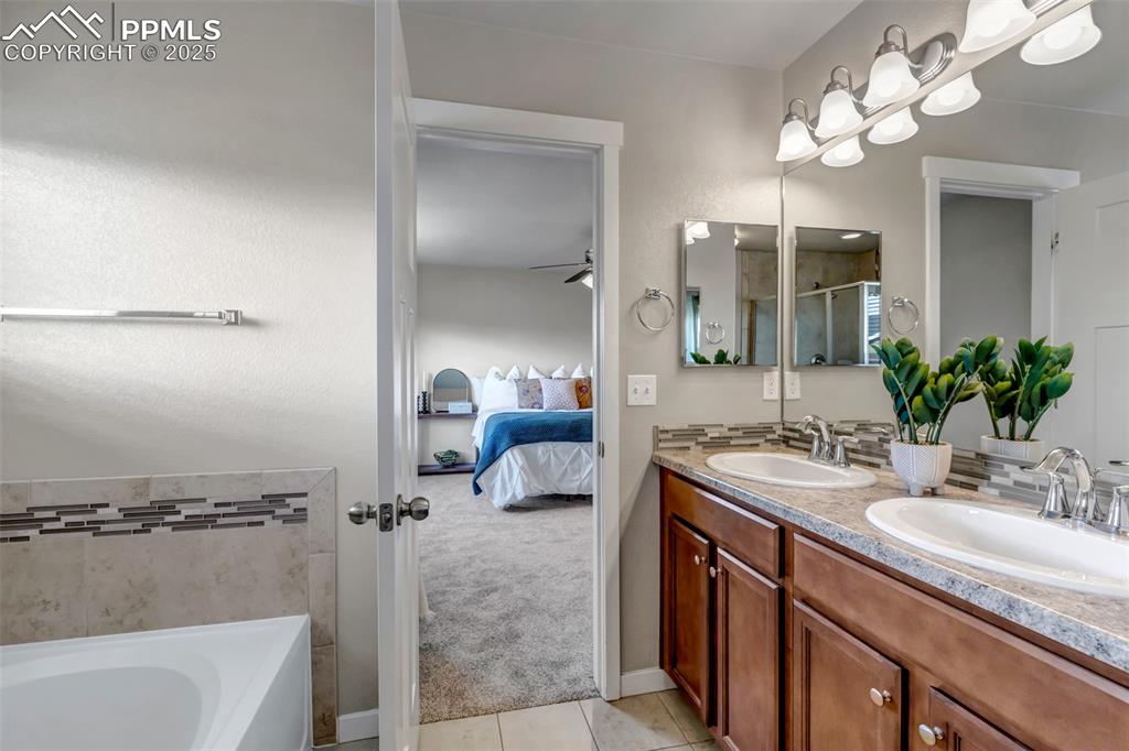 Image 23 of 37: Full bathroom with double vanity, ensuite bathroom, a bath, light tile patt