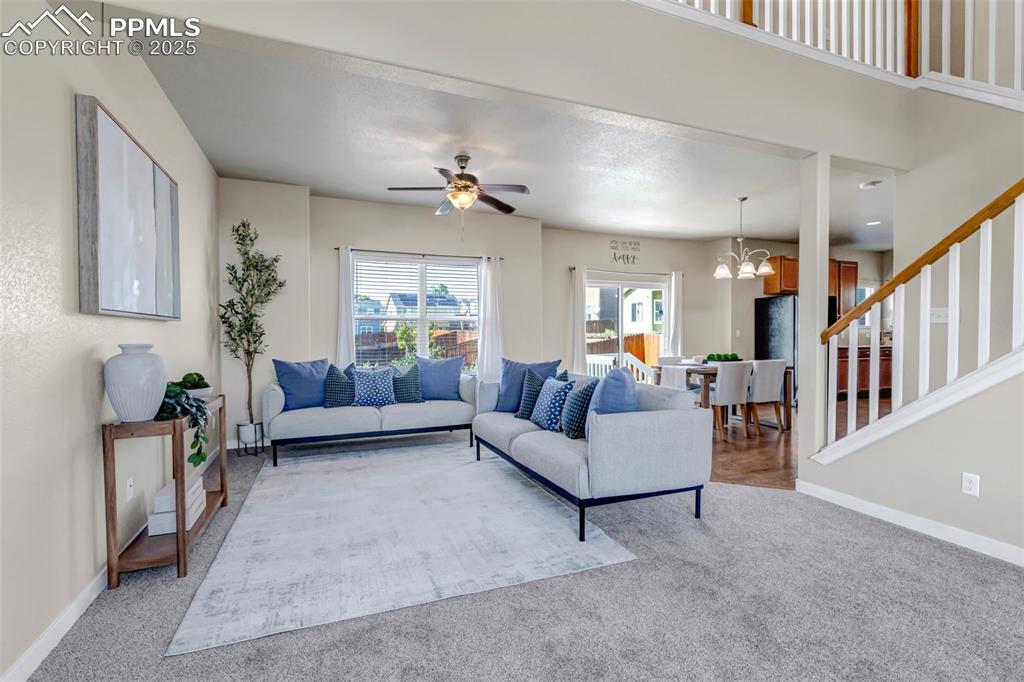 Image 6 of 37: Carpeted living room featuring a ceiling fan, stairway, and a chandelier