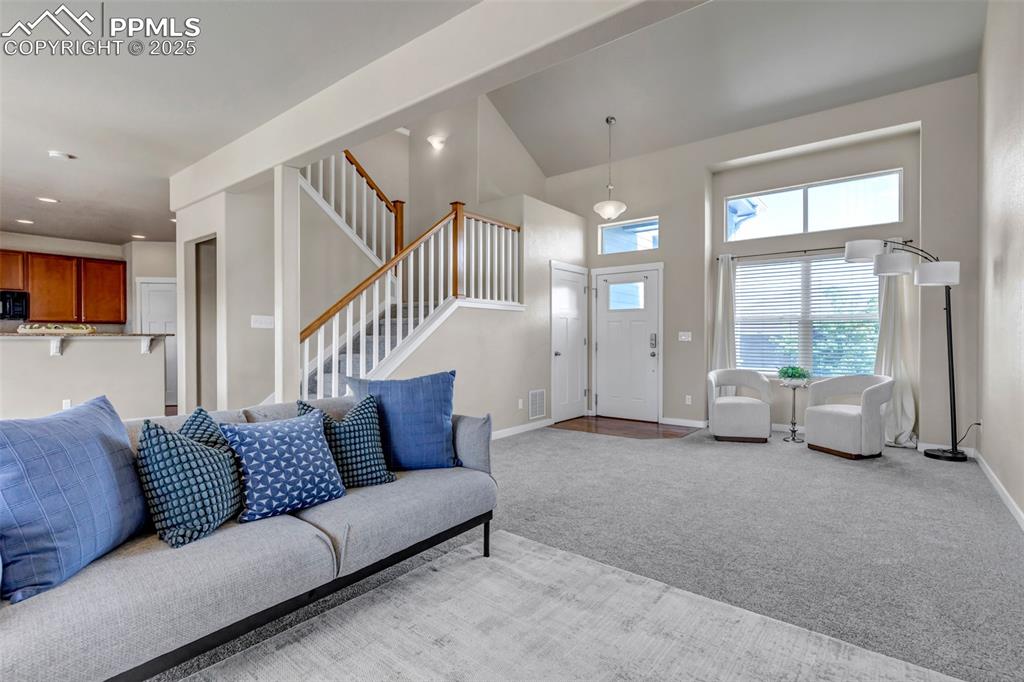 Image 7 of 37: Living room featuring carpet floors, a towering ceiling, and stairs