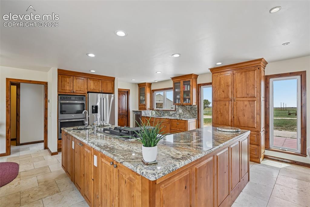 Image 10 of 36: Remodeled kitchen features a large central island with a gas cooktop, grani