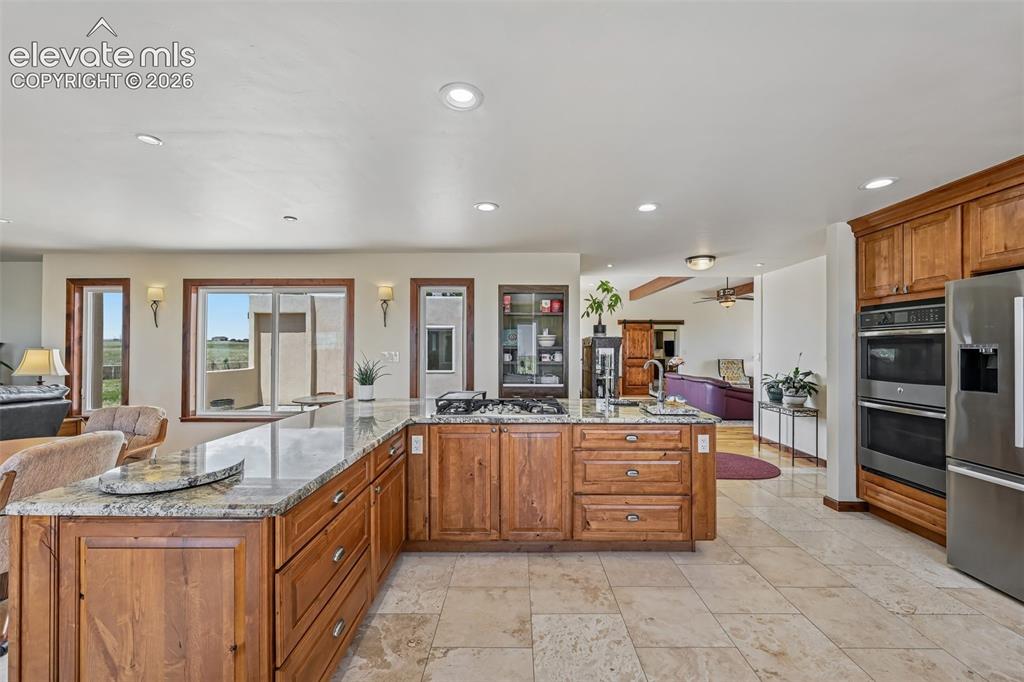Image 15 of 36: Spacious kitchen featuring natural wood cabinetry, light-toned stone tile f