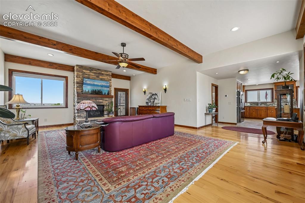 Image 5 of 36: Exposed ceiling beams, hardwood flooring, a stone-clad, gas log fireplace,