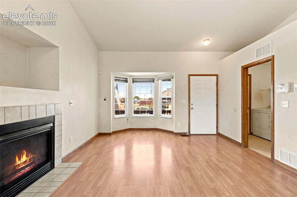 Image 6 of 34: Living area featuring wood-finish flooring, a tiled fireplace, and a bay wi