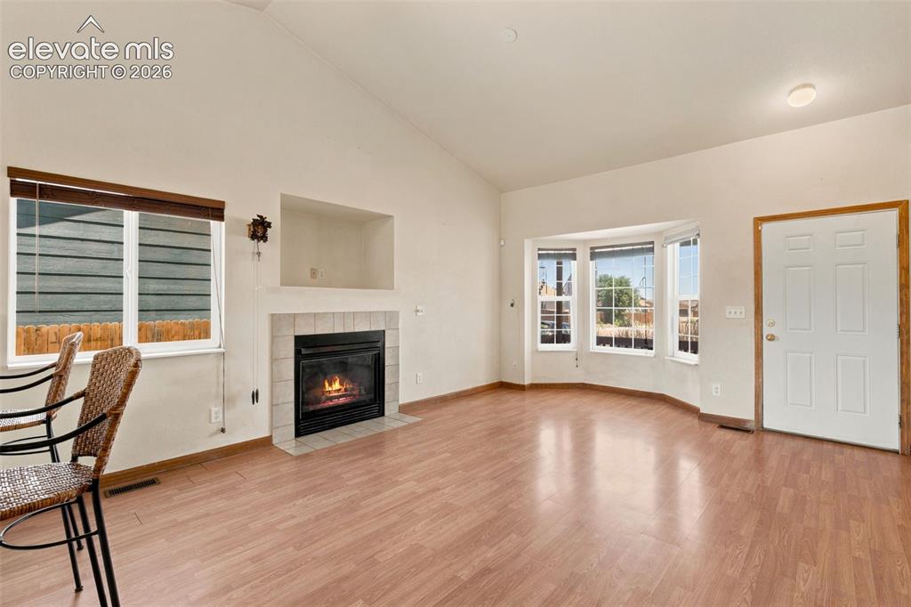 Image 7 of 34: Bright living area featuring wood-finish flooring, a tile-surround fireplac