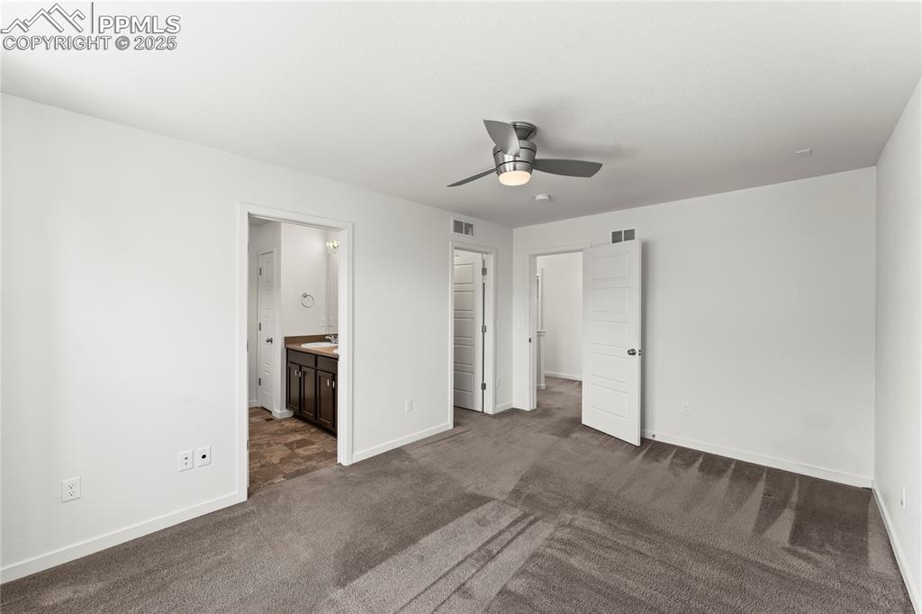 Image 12 of 33: Unfurnished bedroom with dark colored carpet, ensuite bath, and ceiling fan