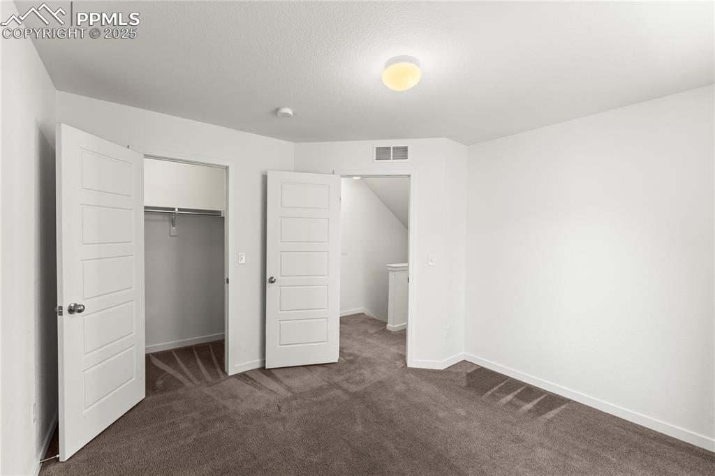 Image 15 of 33: Unfurnished bedroom with dark colored carpet and a walk in closet