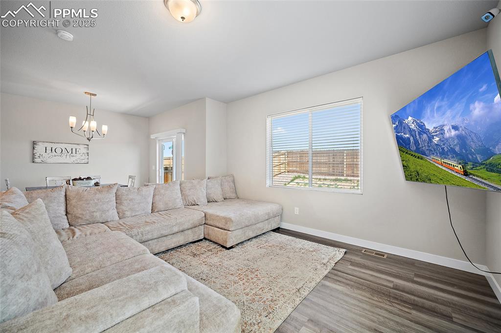 Image 6 of 41: Living area with a chandelier, wood finished floors, and baseboards