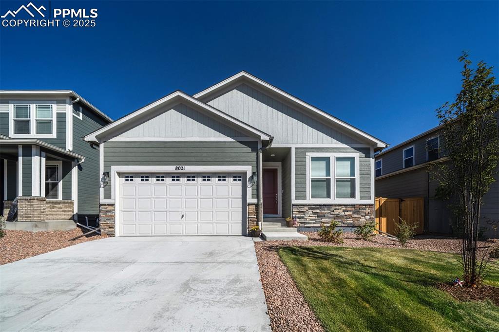 Caption: Craftsman-style house featuring stone siding, concrete driveway, an attached garage, and a front law
