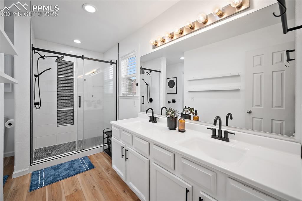 Image 24 of 50: Bathroom with light wood-style floors, a shower stall, double vanity, and r