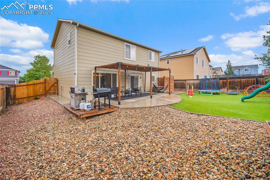 Image 32 of 50: Back of house featuring a fenced backyard, a trampoline, a playground, a re