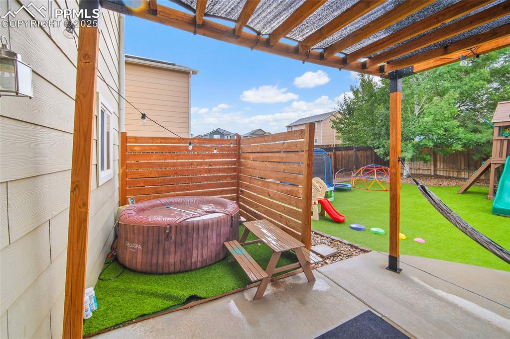 Image 33 of 50: Fenced backyard with a playground, a pergola, and a patio area