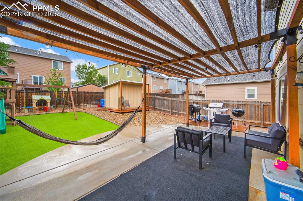 Image 34 of 50: Fenced backyard featuring a playground, a storage shed, a patio area, and a