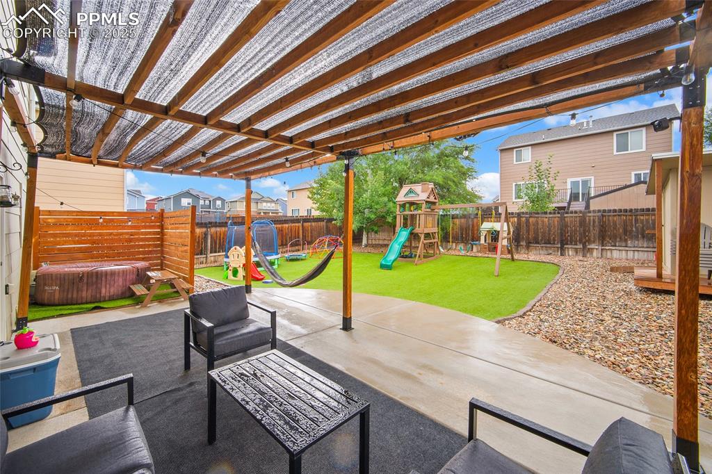 Image 36 of 50: Fenced backyard with a hot tub, a playground, a pergola, and a patio