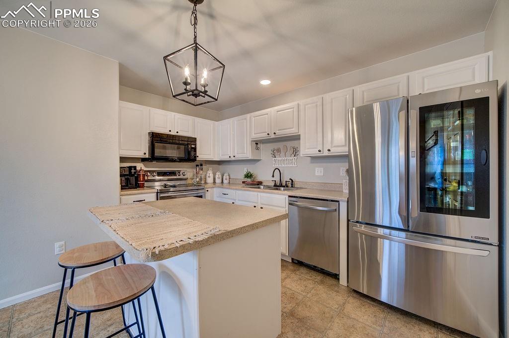 Image 13 of 48: The Island Kitchen features a breakfast bar, white cabinets, modern light f