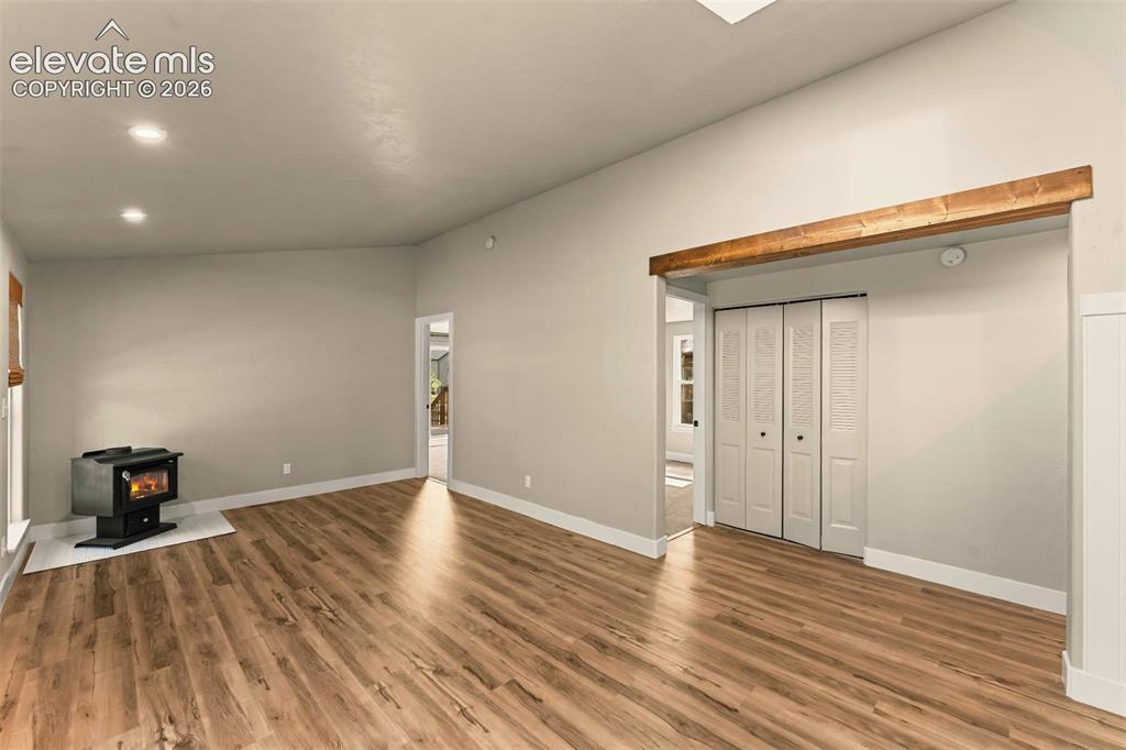 Image 16 of 32: Spacious interior featuring wood-finish flooring, a wood-burning stove on a