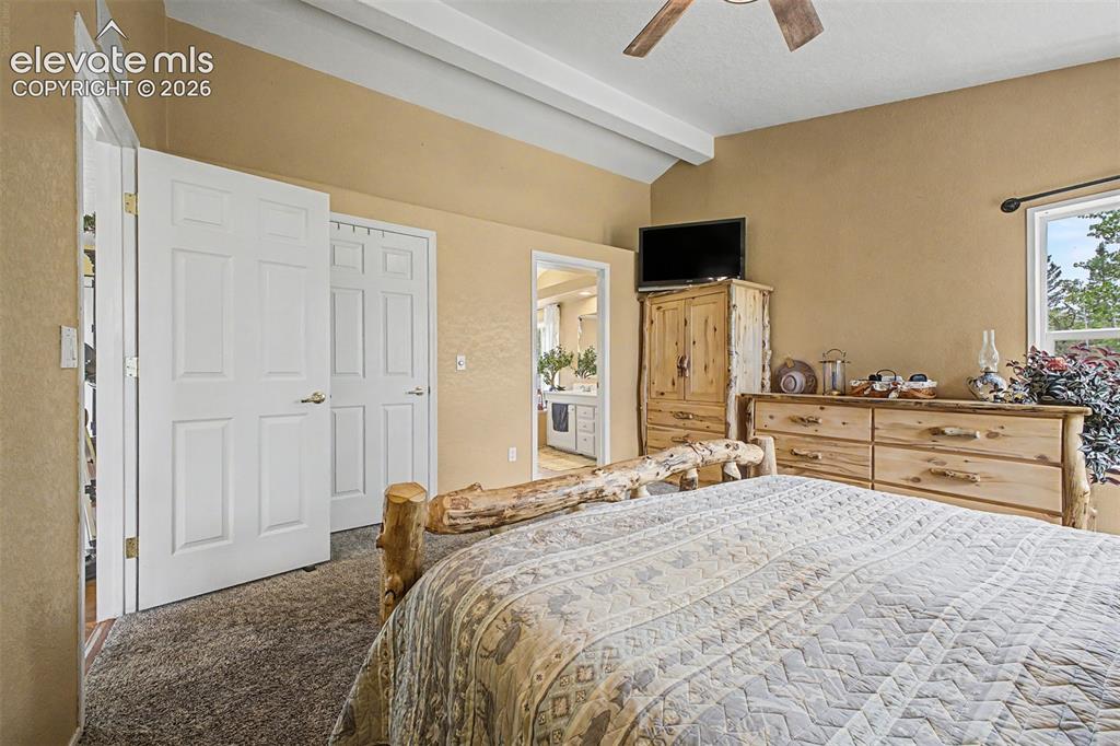 Image 15 of 48: Vaulted ceiling with exposed beam, ceiling fan, and window with dark rod