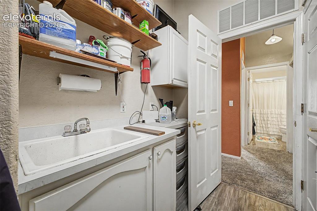 Image 32 of 48: Utility sink with dual faucets, white cabinetry, wood-finish flooring, and 