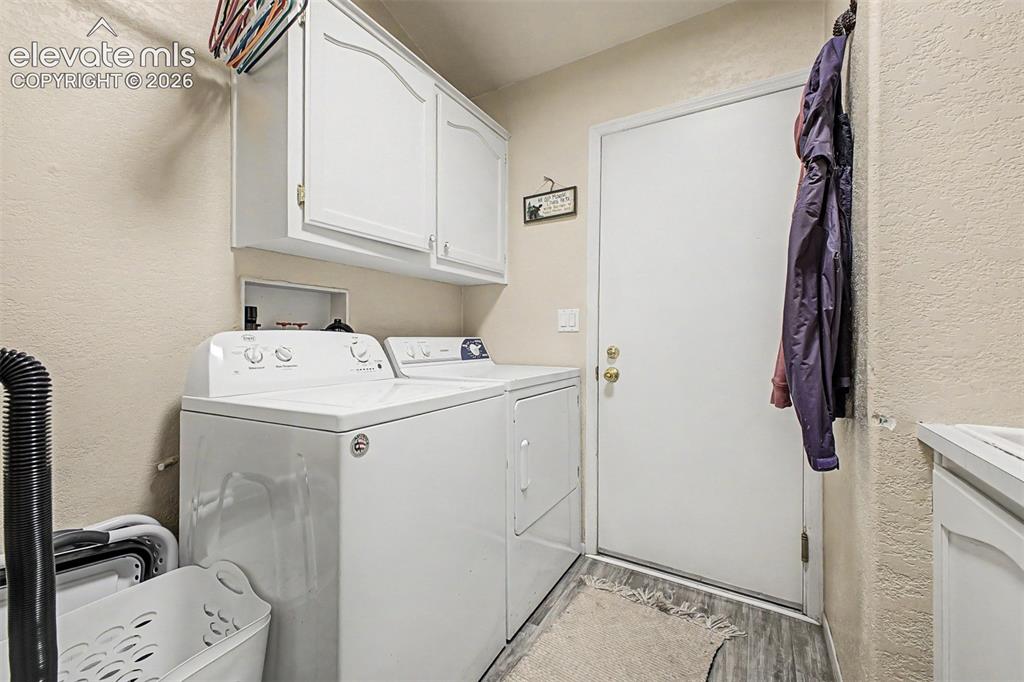 Image 33 of 48: Laundry area featuring upper cabinetry, wood-finish flooring, and a solid e