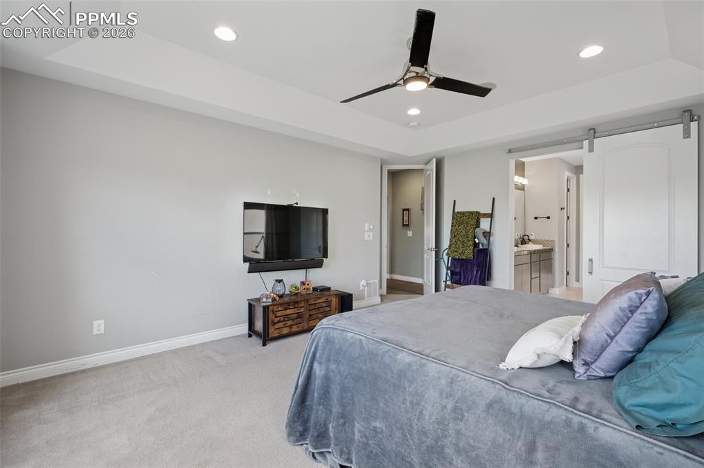Image 21 of 46: Bedroom featuring a tray ceiling, a barn door, baseboards, recessed lightin