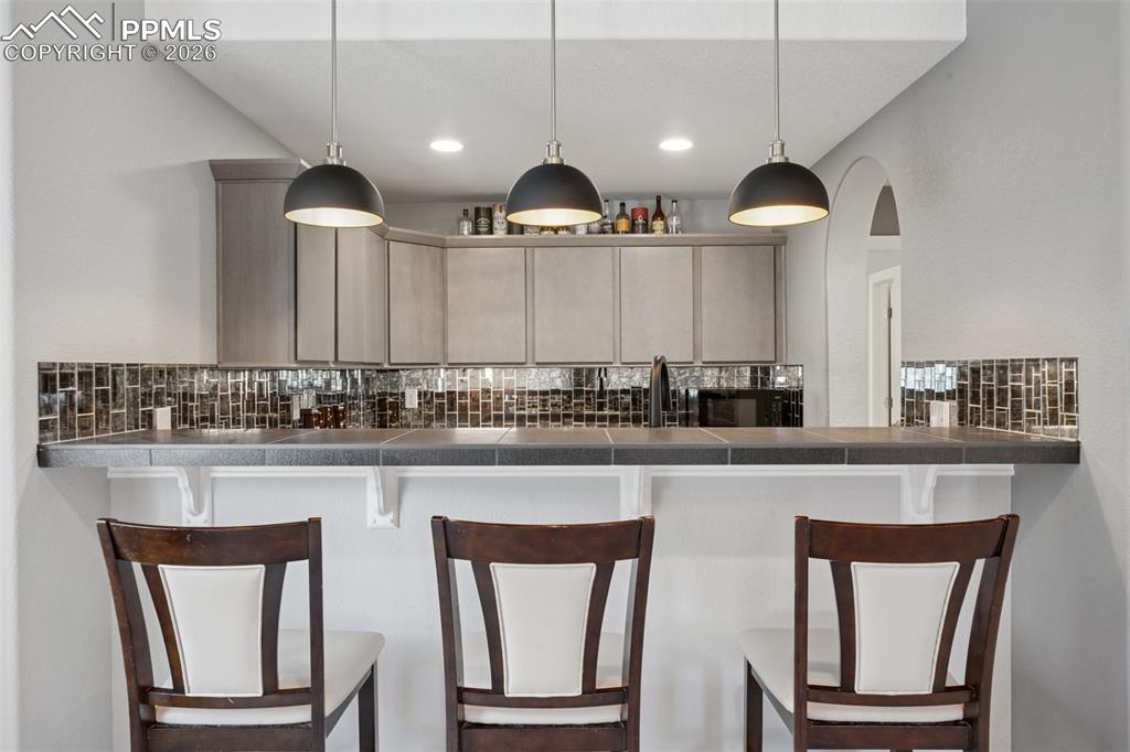 Image 36 of 46: Kitchen featuring backsplash, dark countertops, a kitchen bar, decorative l