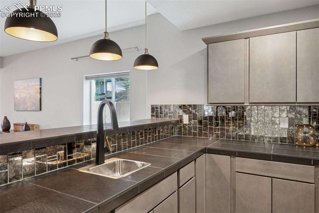 Image 37 of 46: Kitchen featuring a sink, decorative backsplash, dark countertops, and deco