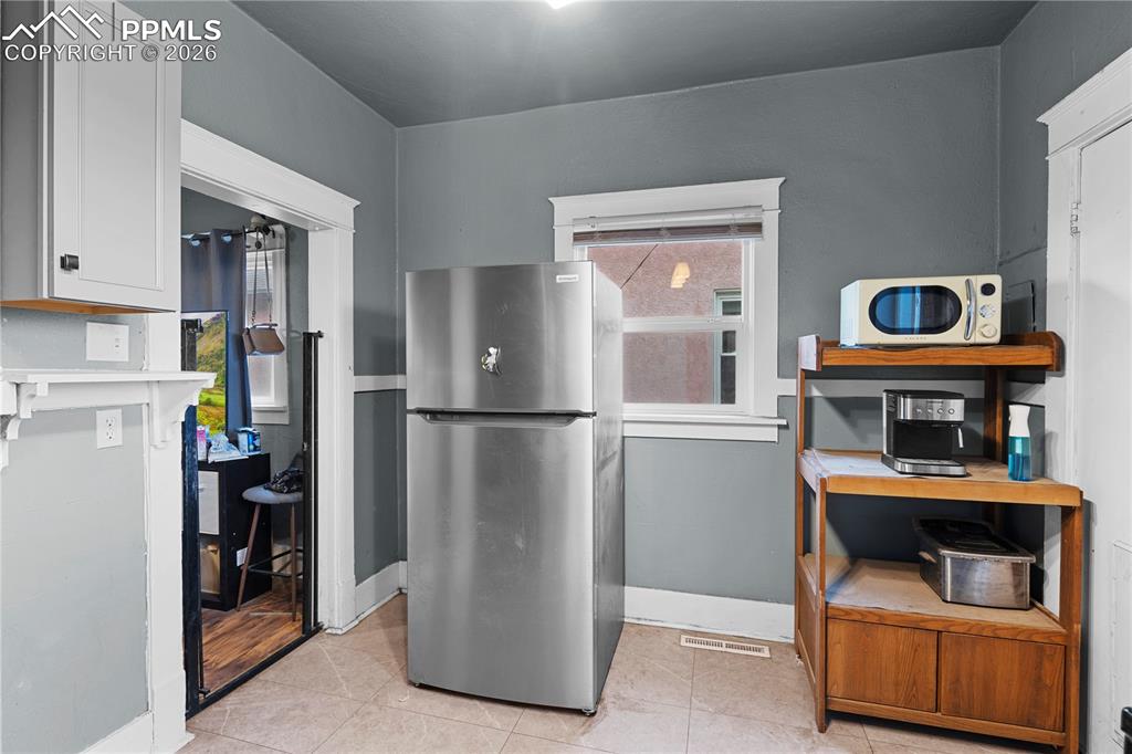 Image 9 of 18: Kitchen featuring freestanding refrigerator, white microwave, light tile pa