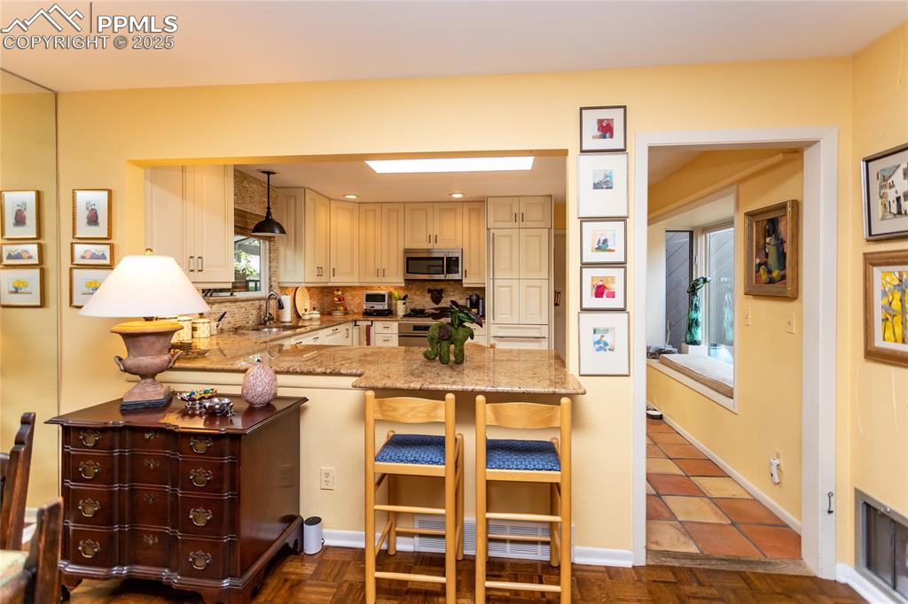 Image 11 of 46: Kitchen with a skylight, light stone counters, a kitchen bar, cream cabinet