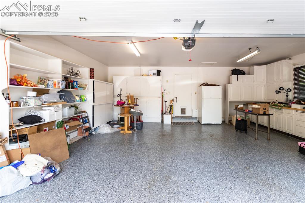 Image 33 of 46: Garage with freestanding refrigerator, storage cabinets, sealed floor and g