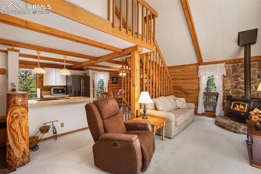 Image 10 of 36: Carpeted living area featuring beamed ceiling, a wood stove, rustic walls,
