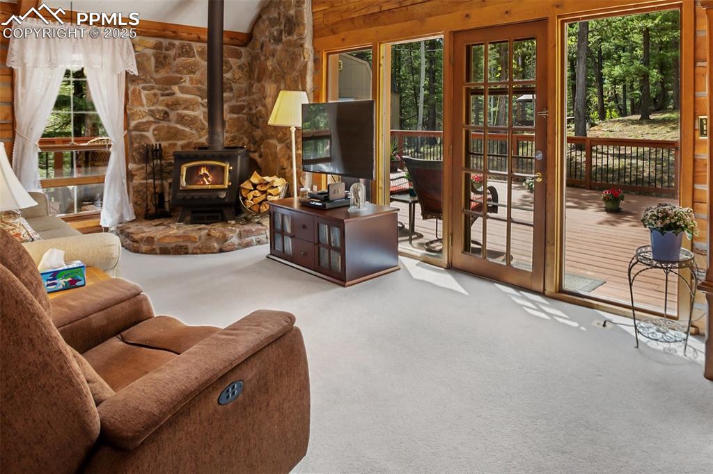 Image 12 of 36: Living room with a wood stove, carpet, and lofted ceiling